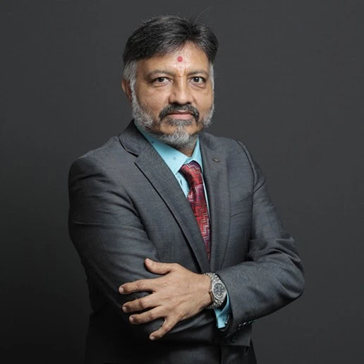 Sanjay Ajmera, Whole-Time Director of Ajmera Realty and Infra India Ltd., photographed standing in a grey suit against a dark studio background.